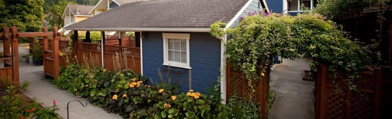 A small blue house with a wooden fence and a walkway leading to it.