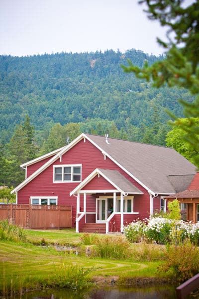 A red house with a pond in front of it and mountains in the background