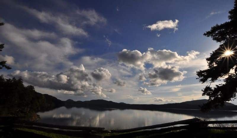 The sun is shining through the clouds over a lake