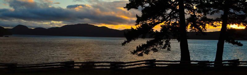 A sunset over a lake with trees in the foreground and mountains in the background.