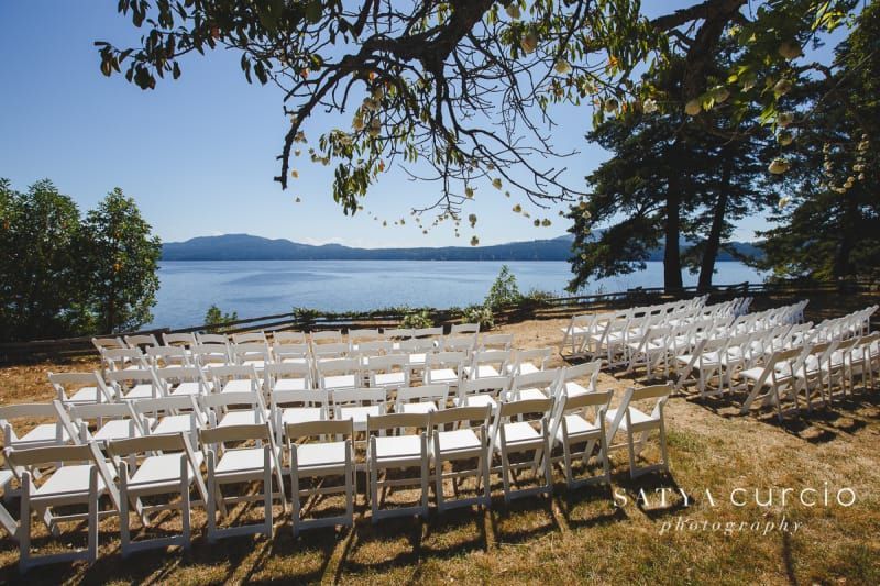 A row of white chairs are lined up in front of a lake