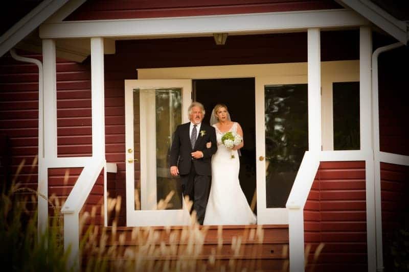 A bride and her father are standing in front of a red house