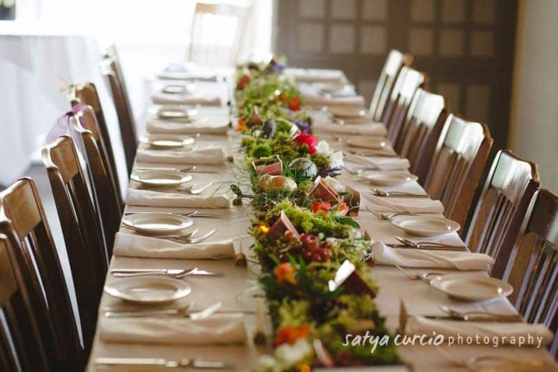 A long table with plates , silverware , and flowers on it.