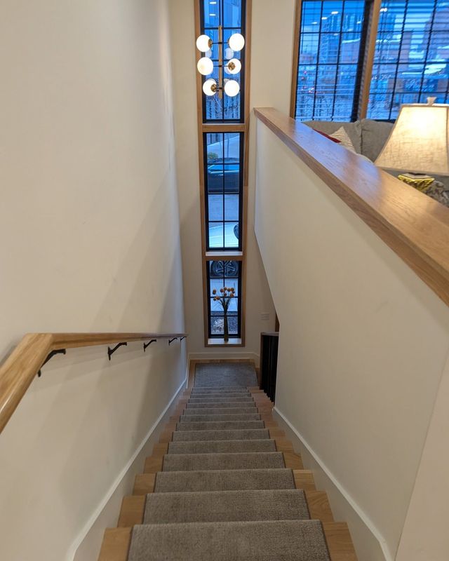 Staircase descending between beige walls with a window at the landing and blue sky outside