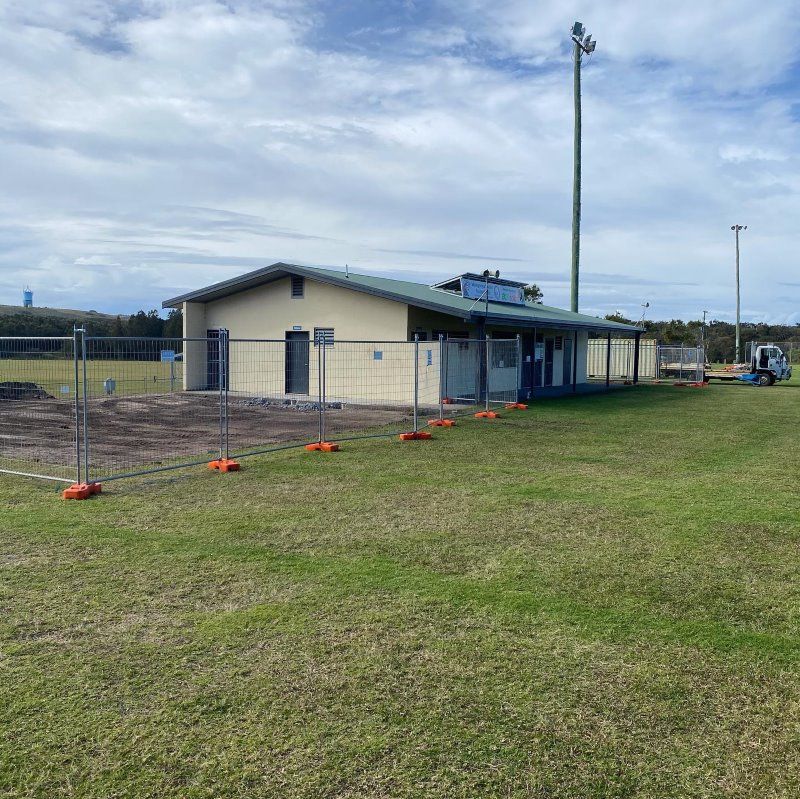 A Building Is Being Built In A Grassy Field Behind A Fence — Coffs Temporary Fencing Pty Ltd In Moonee Beach, NSW