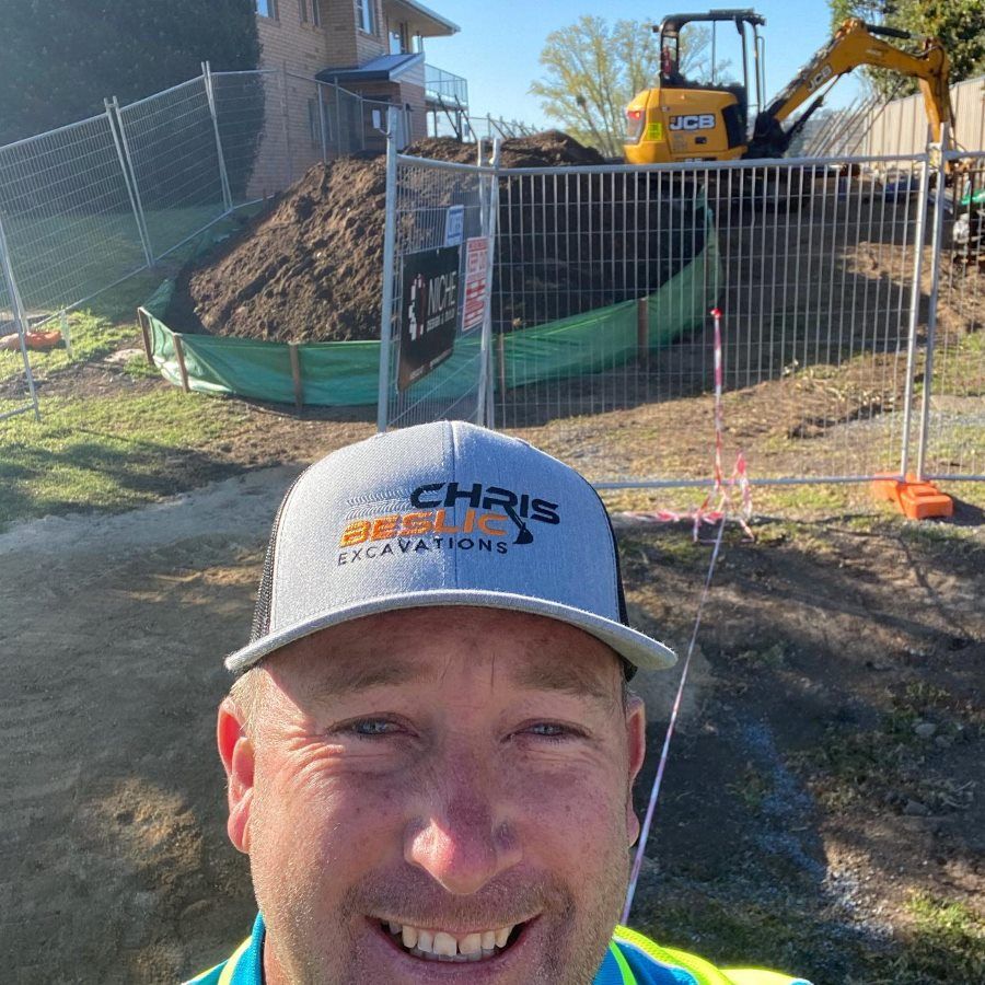 A Man Wearing A Hat Is Smiling In Front Of A Construction Site — Coffs Temporary Fencing Pty Ltd In Moonee Beach, NSW