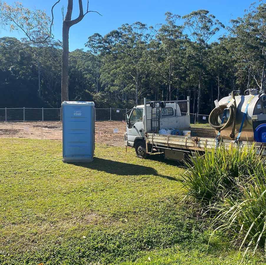 A Truck Is Parked In The Grass Next To A Portable Toilet — Coffs Temporary Fencing Pty Ltd In Moonee Beach, NSW