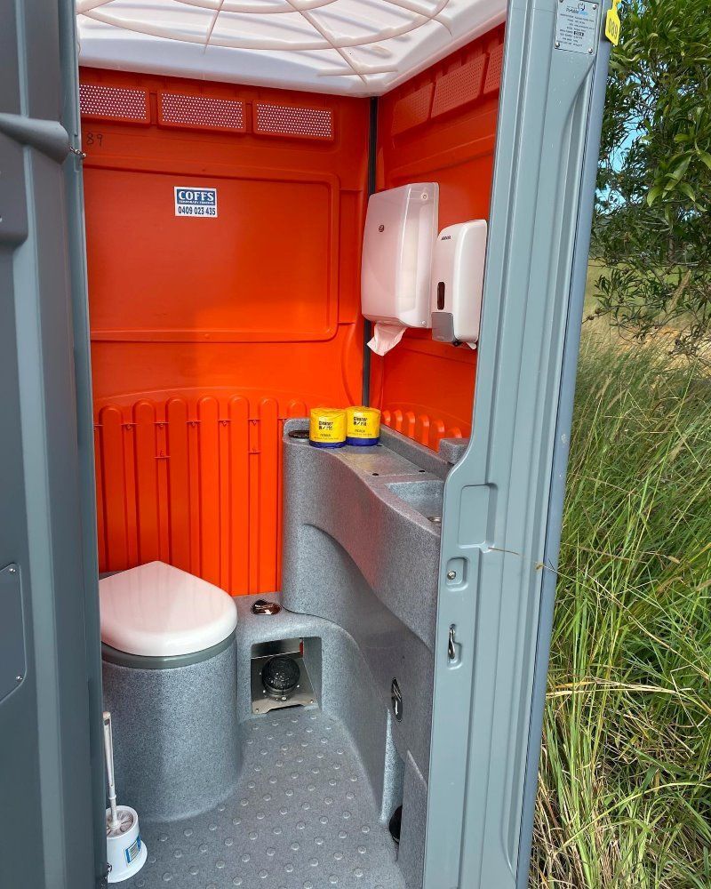 A Portable Toilet With An Orange Wall And A Sink — Coffs Temporary Fencing Pty Ltd In Moonee Beach, NSW