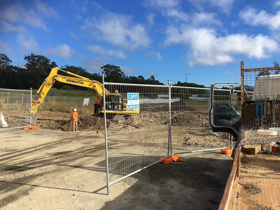 A Construction Site With A Yellow Excavator Behind A Fence — Coffs Temporary Fencing Pty Ltd In Macksville, NSW