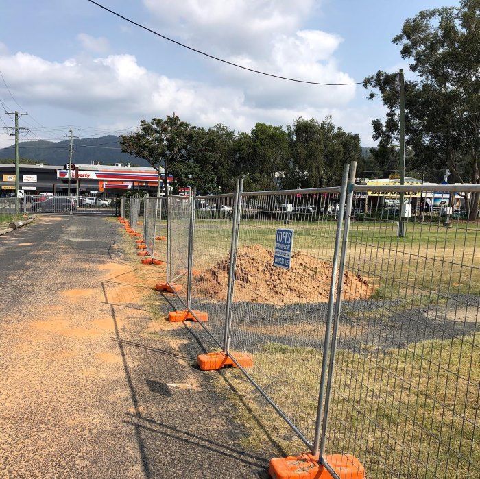A Fence Is Sitting On The Side Of A Road Next To A Dirt Road — Coffs Temporary Fencing Pty Ltd In Bellingen, NSW