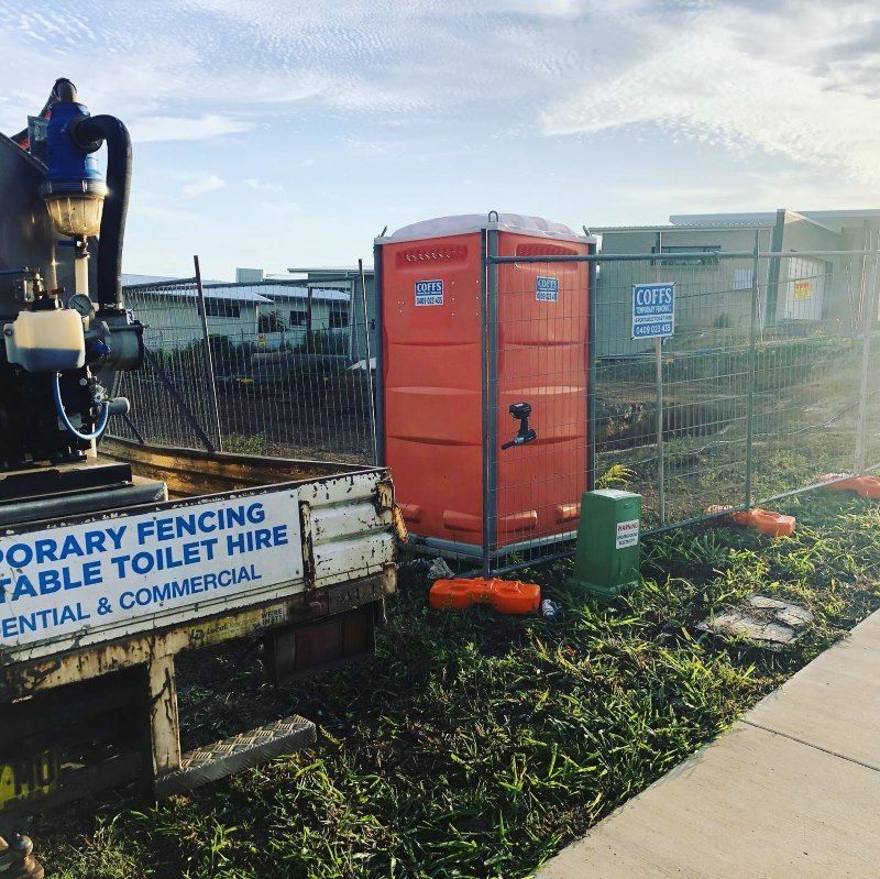 A Portable Toilet Is Sitting Next To A Truck — Coffs Temporary Fencing Pty Ltd In Macksville, NSW