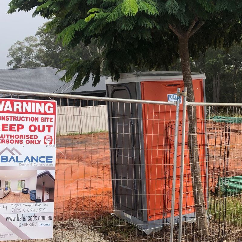 An Orange Portable Toilet Is Behind A Fence With A Warning Sign — Coffs Temporary Fencing Pty Ltd In Moonee Beach, NSW