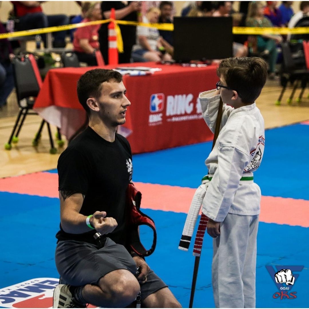 A man kneeling down talking to a young boy in a karate uniform