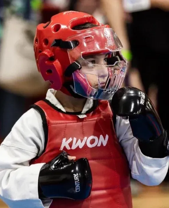 A young boy wearing a red kwon vest and black boxing gloves