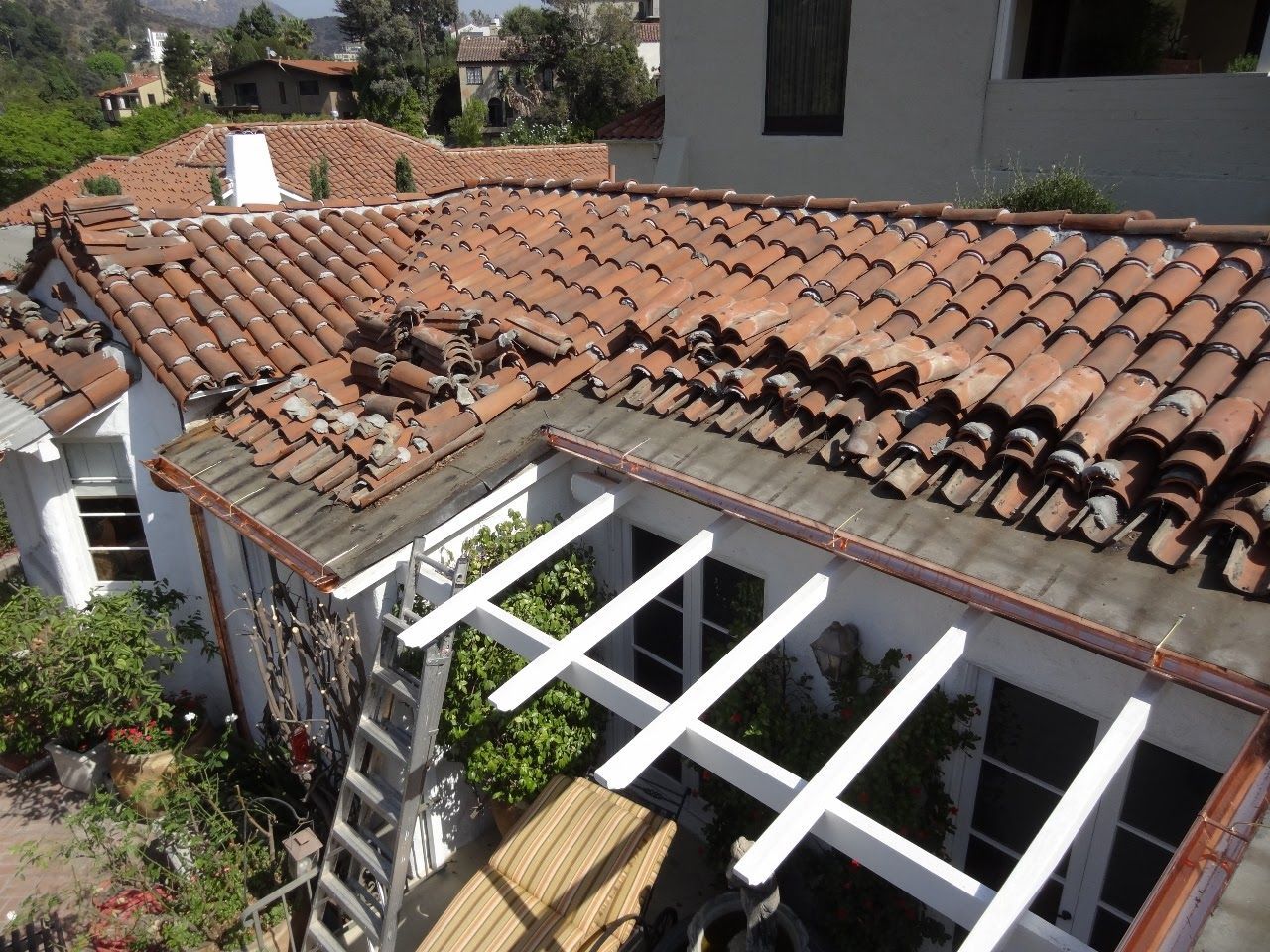 Rooftop with damaged terracotta tiles, white pergola, and ladder against the building.