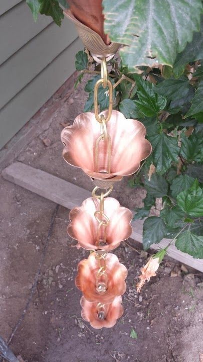 Copper flower-shaped rain chain hanging outdoors, partially obscured by green foliage.