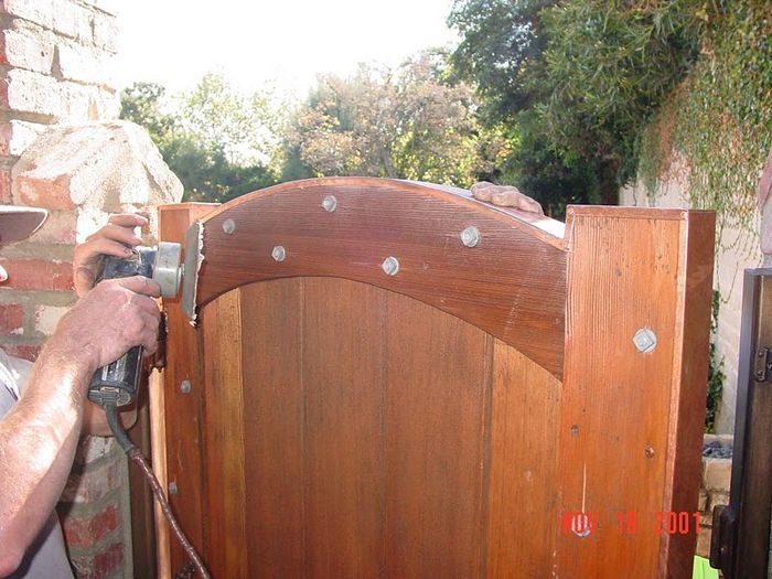 Person sanding a wooden gate with a power sander outdoors.