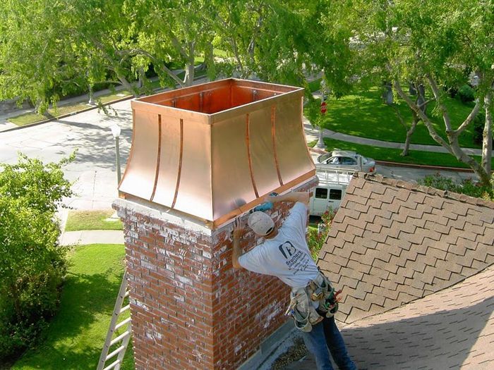 Roofer in white shirt installing copper chimney cap on brick chimney. Sunny day, residential area.