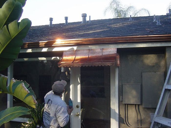 Man installing copper awning over a doorway, under a roof with copper gutters.