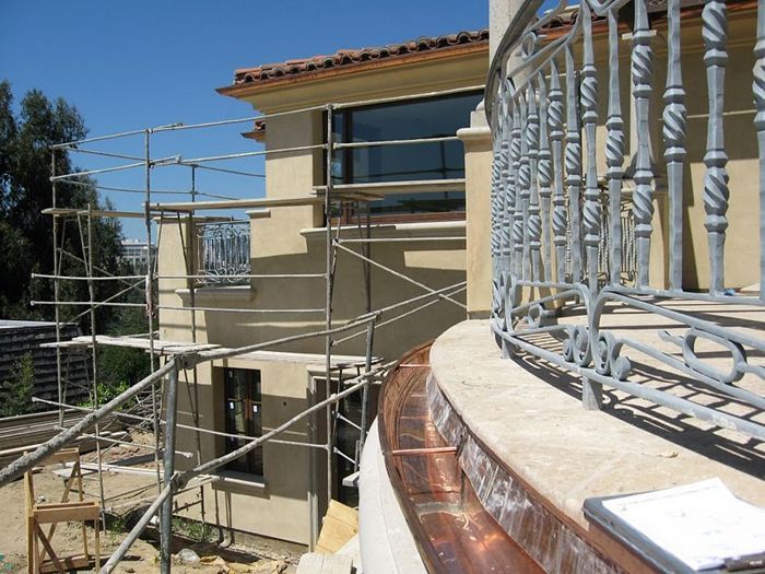 Exterior of a house with scaffolding.  A curved balcony with decorative railing is visible in the foreground.