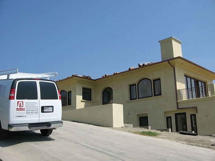 White van parked on driveway in front of a light yellow two-story house with a blue sky.