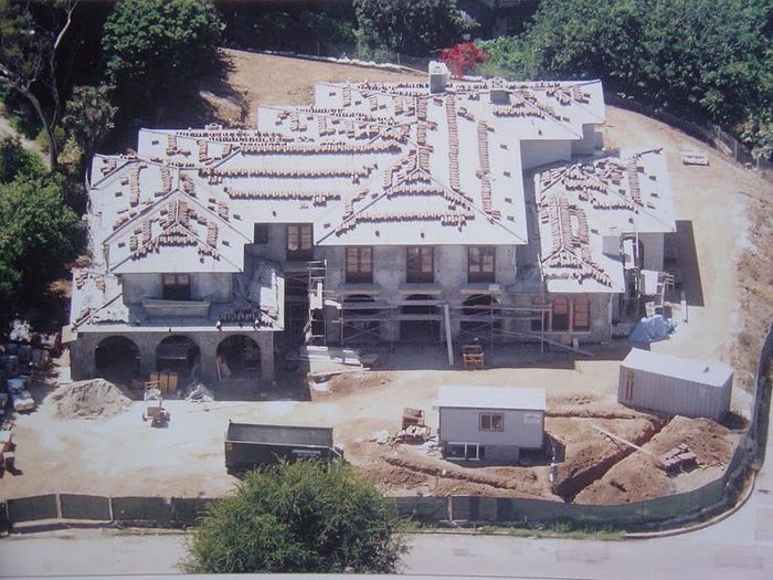 Large house under construction; roof tiles being laid; dirt and construction materials surround.
