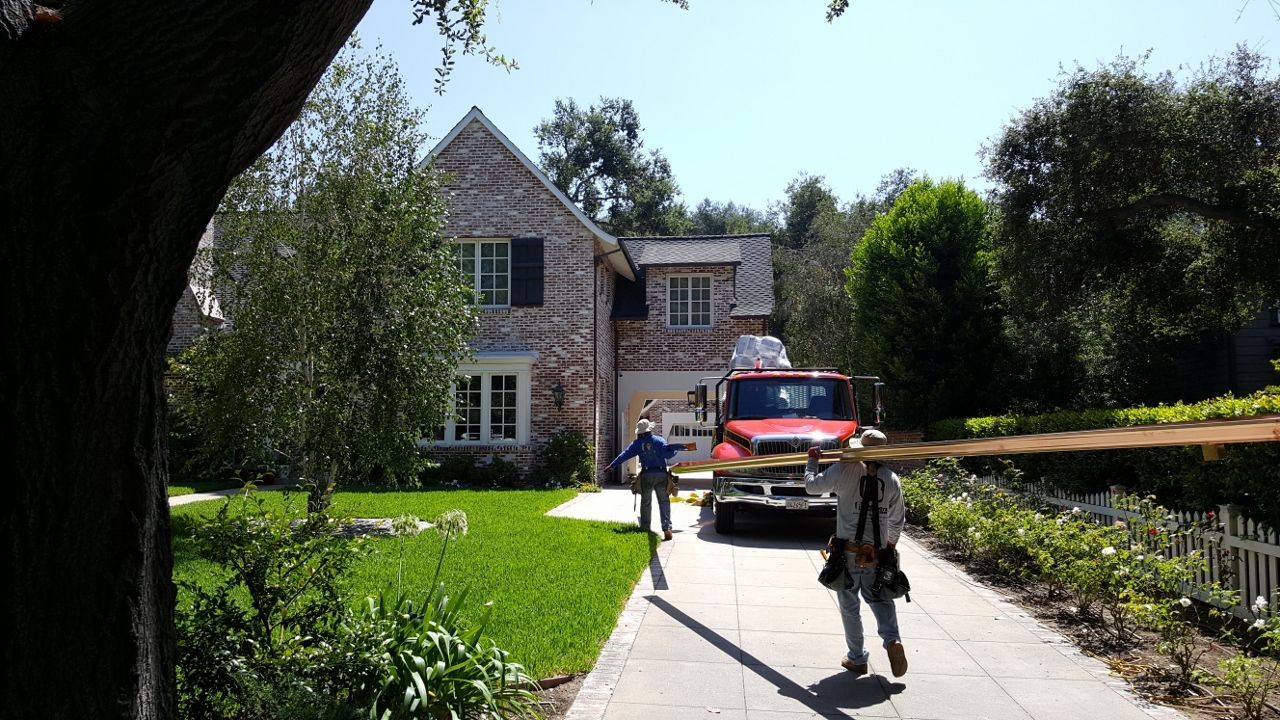 A red fire truck parked in front of a brick house; two people run towards it on a sunny day.
