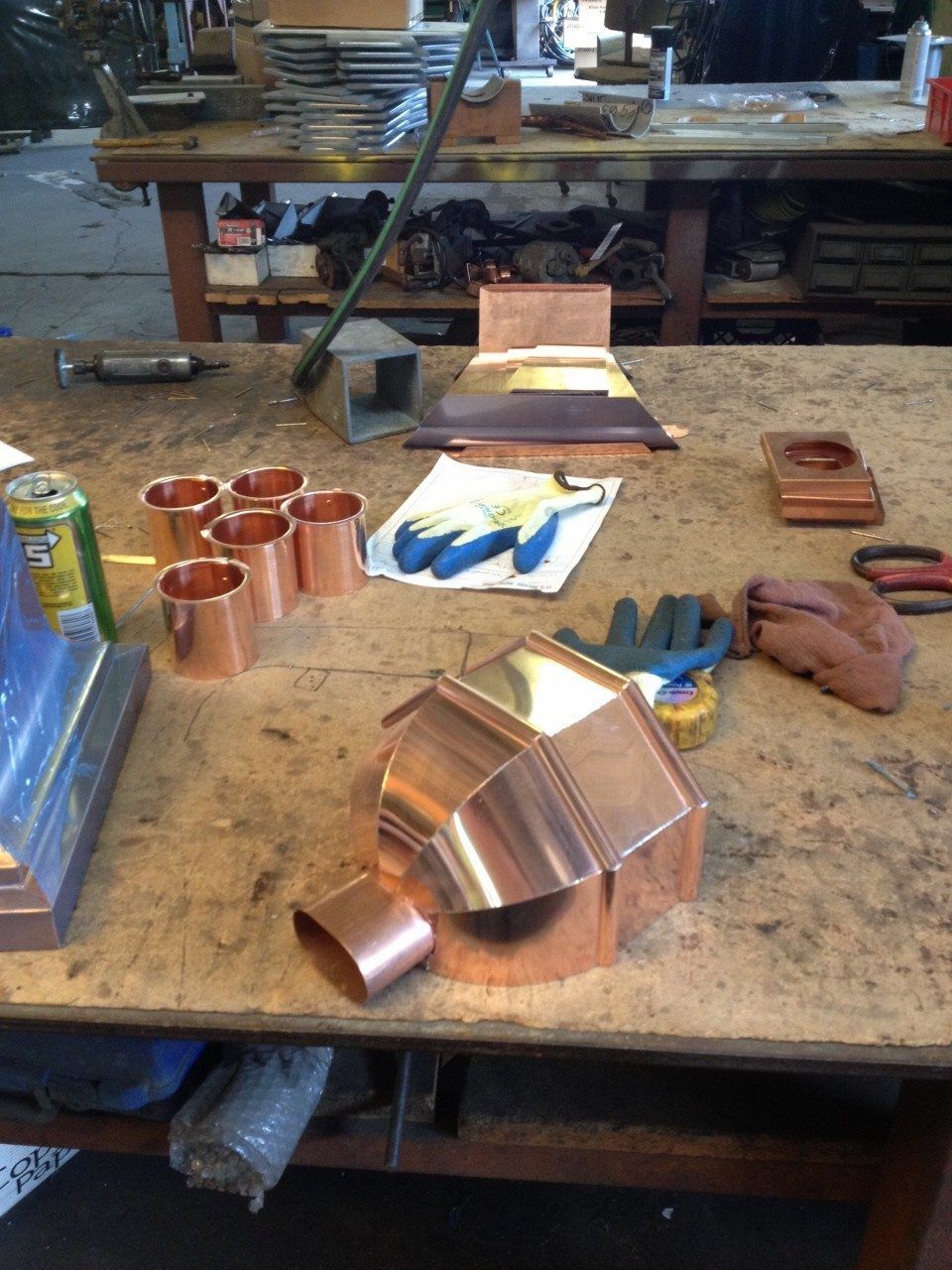 Copper pieces in various stages of construction on a workbench, with tools and materials nearby.