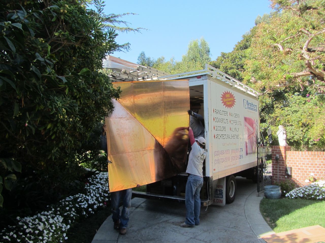 Two people opening the side door of a truck parked on a driveway, next to a house.