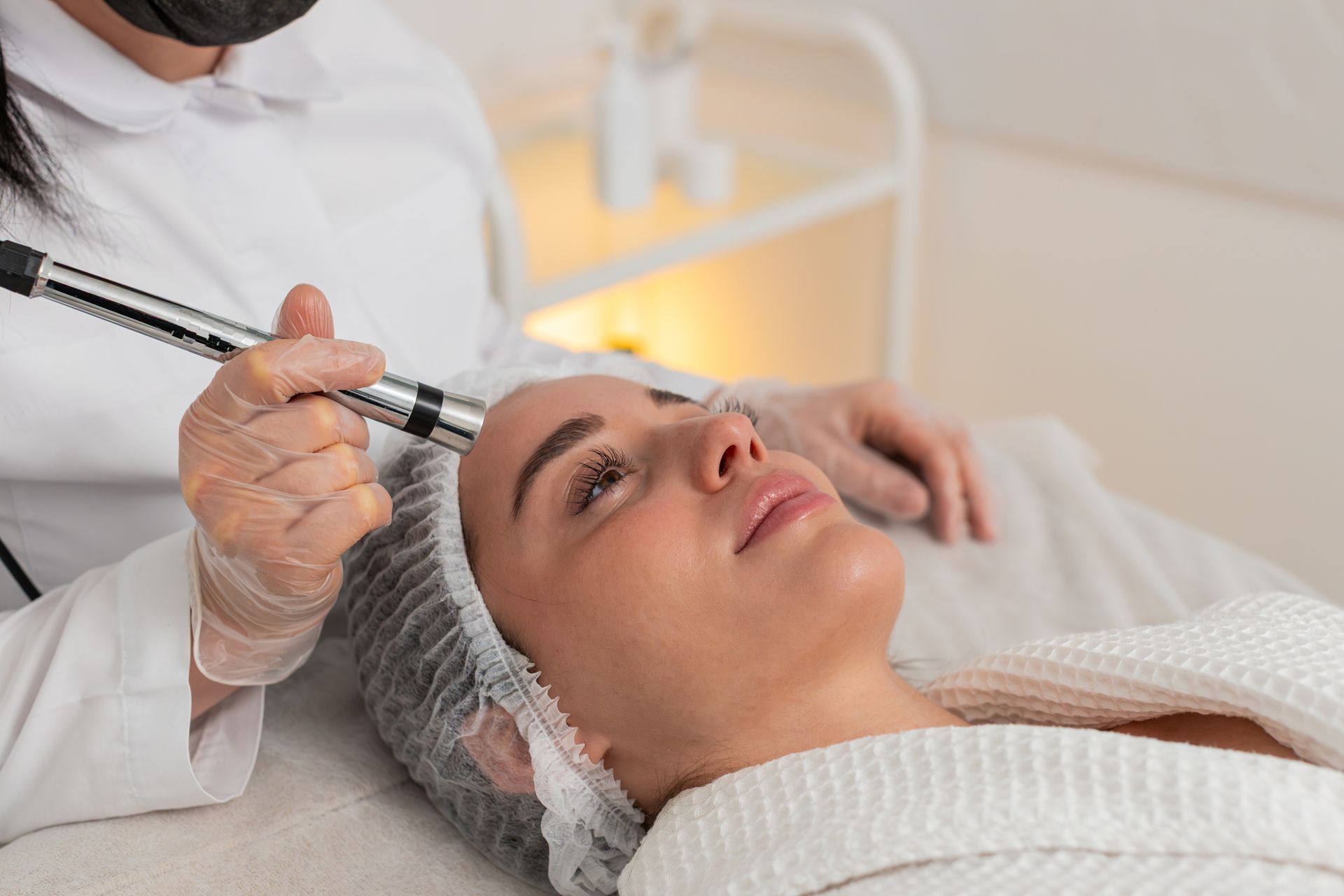 Trattamento cosmetico applicato sulla fronte di una cliente sdraiata sotto un asciugamano bianco.
