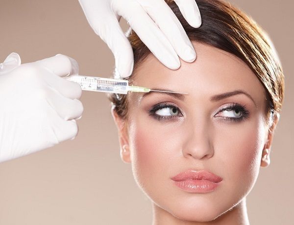 Mani guantate iniettano una siringa nella fronte di una donna mentre lei guarda altrove.