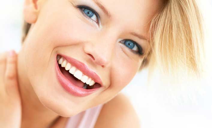 Donna bionda sorridente con occhi azzurri su uno sfondo bianco brillante