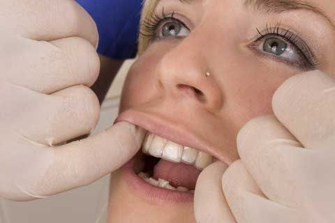 Un dentista con i guanti esamina i denti di un paziente sorridente con strumenti odontoiatrici.