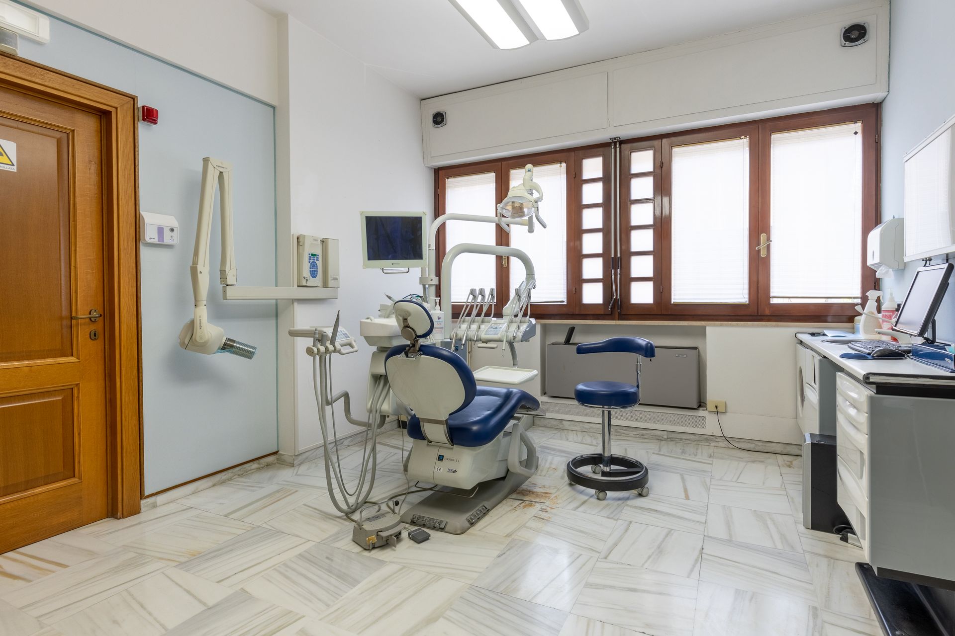 Sala ambulatoriale odontoiatrica con poltrona per visite, strumenti, lavandino e finestre.