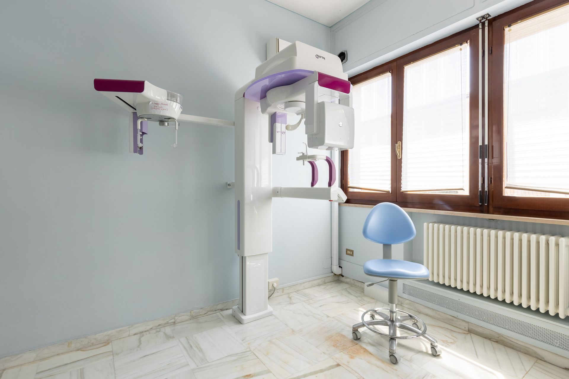 Sala odontoiatrica con apparecchio radiografico panoramico, poltrona per la visita e ampie finestre.