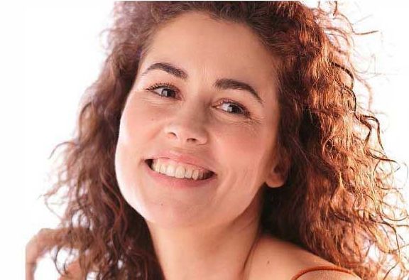Persona sorridente con capelli ricci color castano ramato su uno sfondo bianco brillante