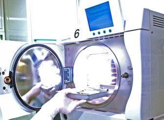 Una persona carica degli oggetti in uno sterilizzatore in acciaio inossidabile con sportelli circolari aperti