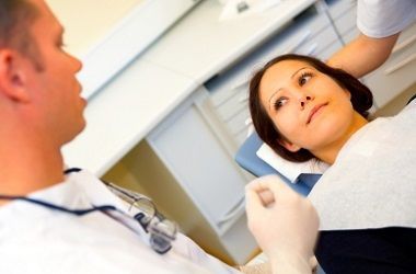 Paziente sdraiato su una poltrona odontoiatrica mentre il dentista parla in una clinica luminosa