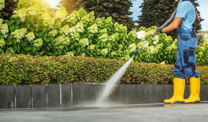 A man is using a high pressure washer to clean a sidewalk.