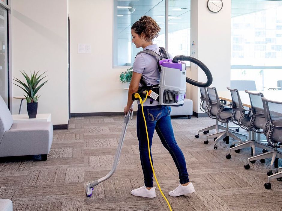 A woman is cleaning the floor with a vacuum cleaner.