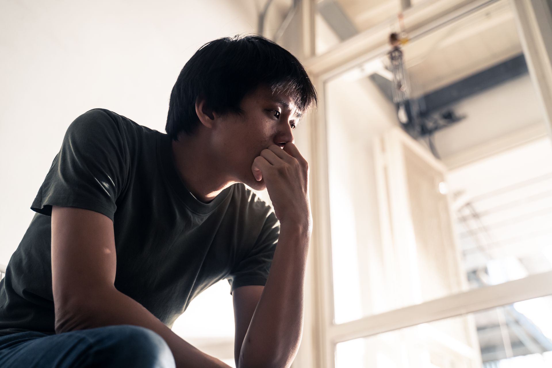 A man is sitting in front of a window with his hand on his face.