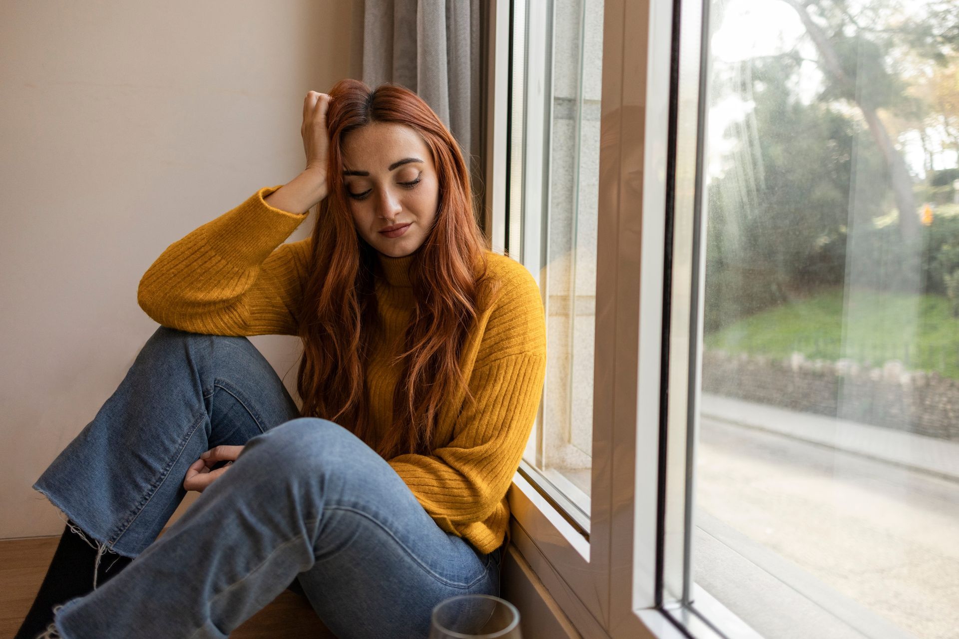 Woman sitting by a window in soft morning light, considering whether to take anxiety medication