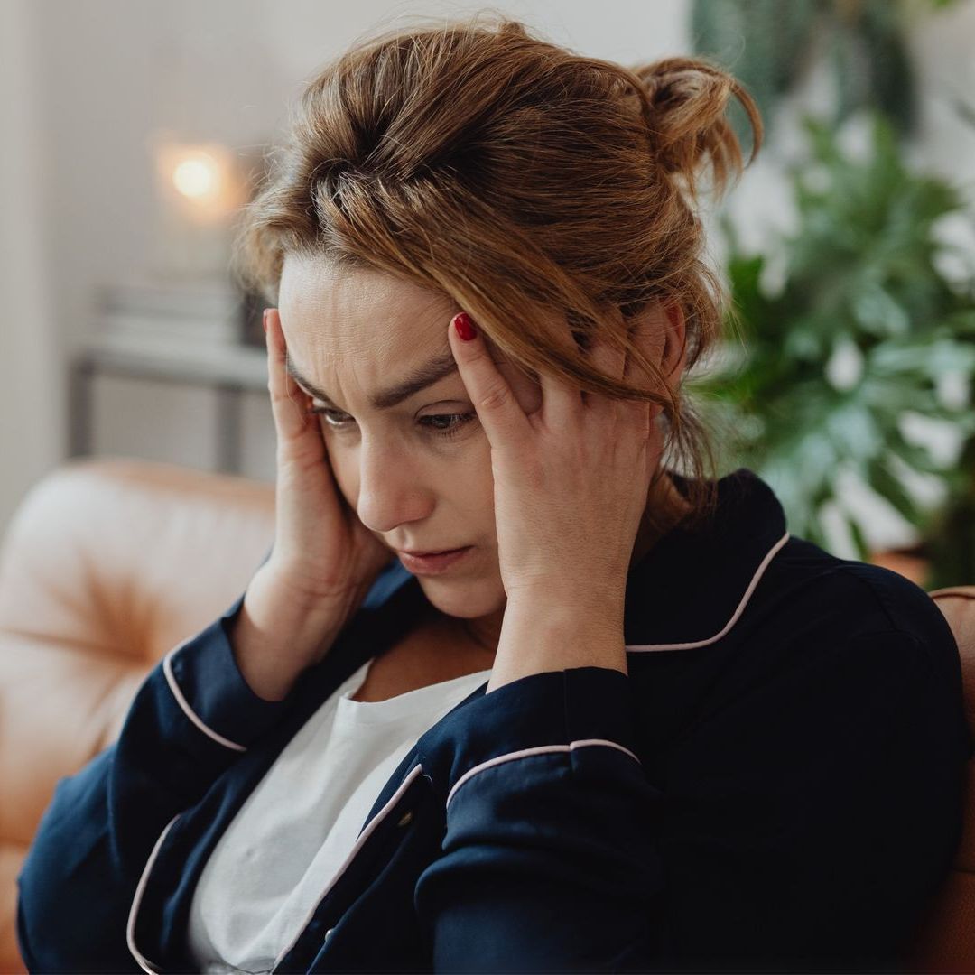 A man is sitting on a couch with his hands on his face.