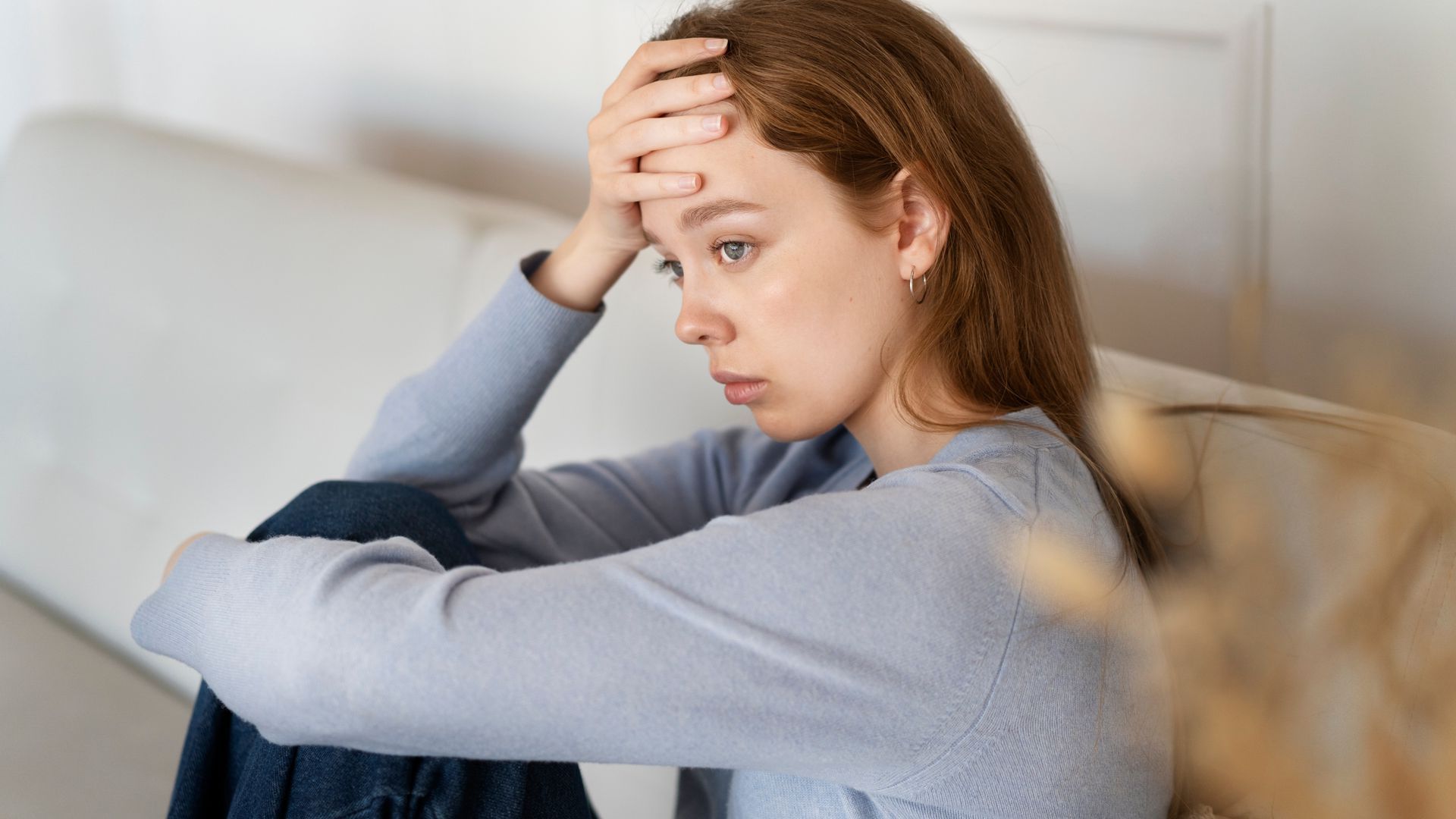 A woman is sitting on a couch with her head in her hands.