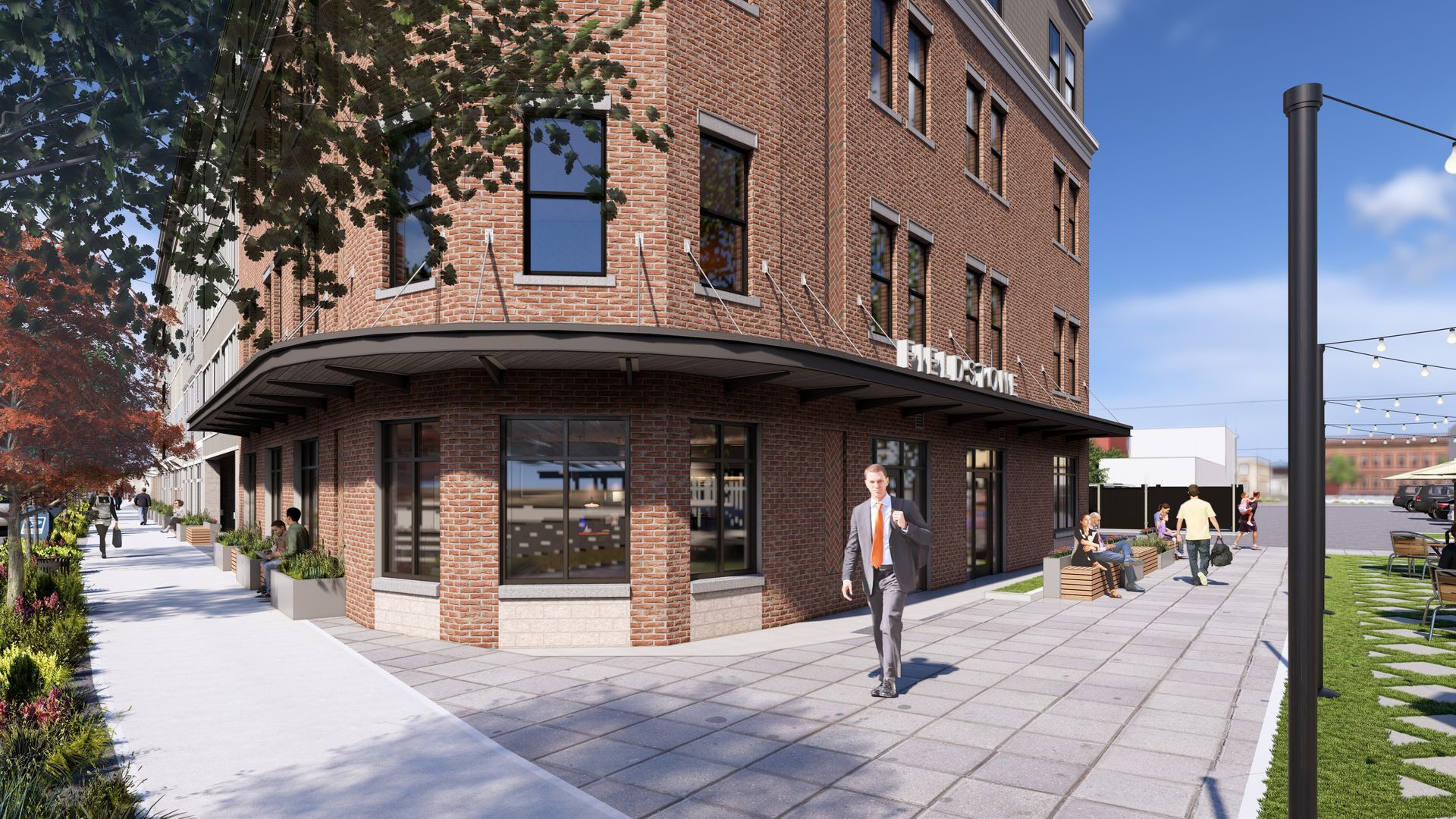 A brick building on a corner with a sidewalk, outdoor seating, and a person walking towards the entrance.