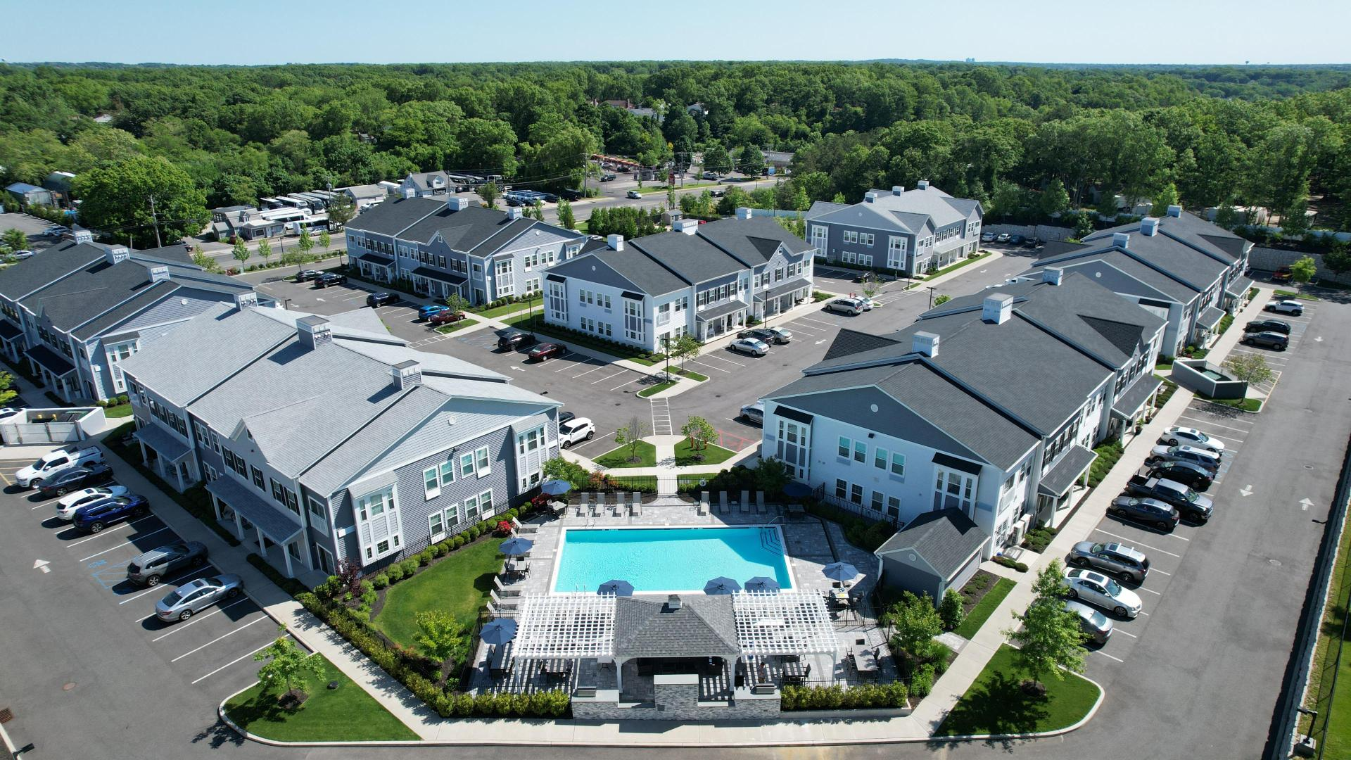Aerial view of a residential apartment complex featuring multiple grey buildings, a swimming pool, and parking areas.
