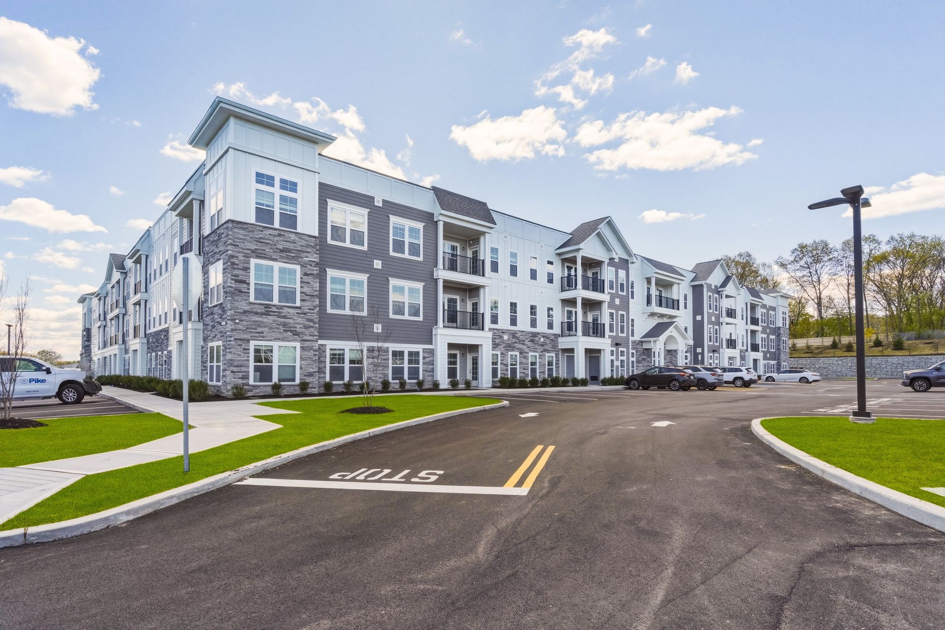 A newly constructed multi-story apartment building with stone and white siding, under a clear blue sky.