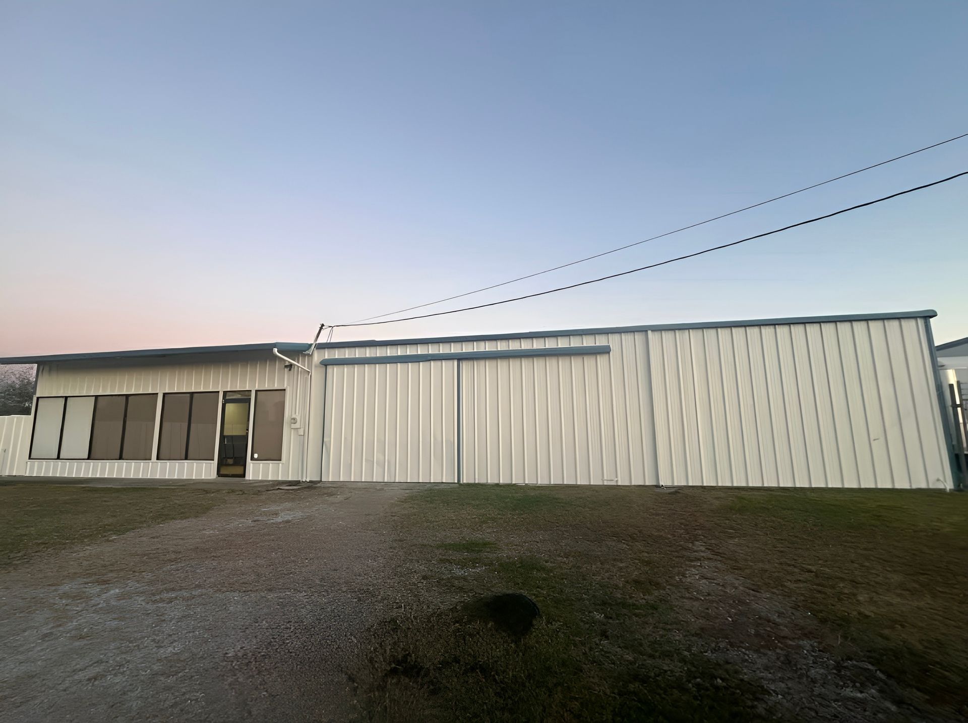 Long white metal building at dusk with a small covered porch and gravel foreground