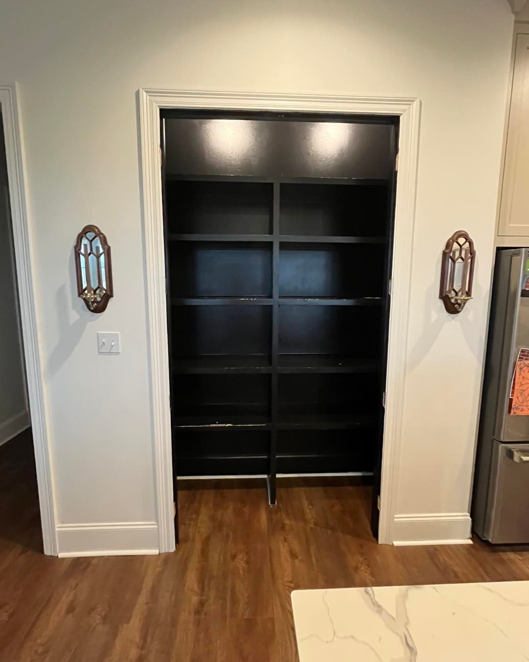 Open doorway to a built-in black shelving closet in a room with hardwood floors and white trim