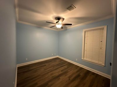 Empty light-blue bedroom with wood floor, ceiling fan, and a window with white blinds.